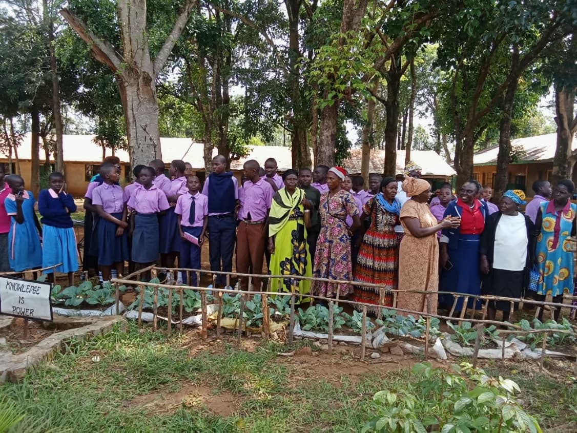 Green Clubs students, teachers, and community members gathered around the school kitchen garden with 'Knowledge is Power' banner